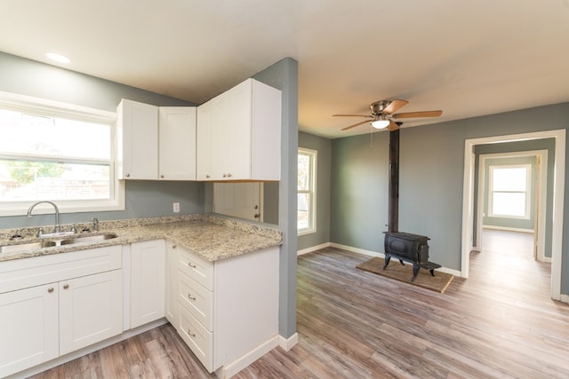kitchen featuring a ceiling fan, a wood stove, a sink, white cabinets, and light wood-style floors