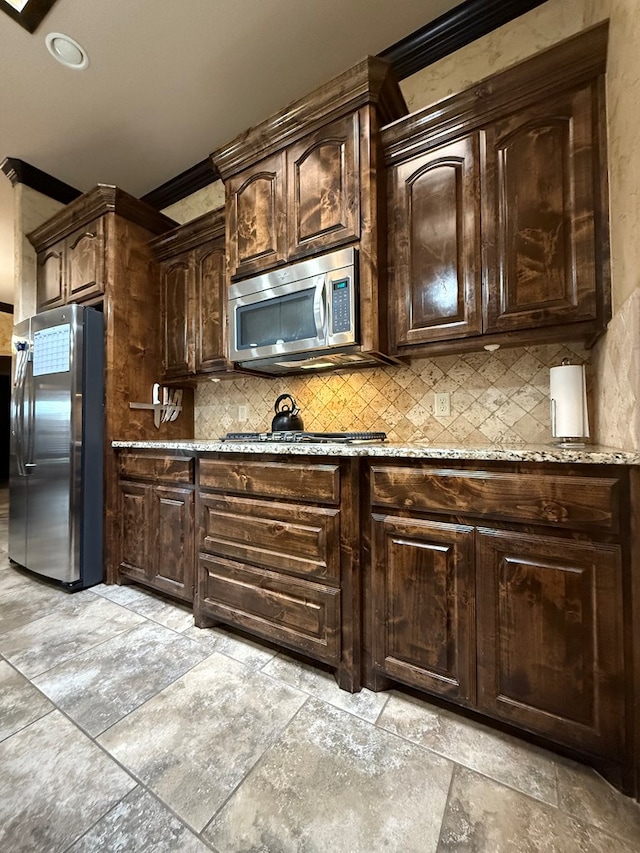 7802 Sienna Dr, Odessa, TX 79765 - kitchen featuring appliances with stainless steel finishes, tasteful backsplash, light stone counters, stone tile floors, and dark brown cabinets