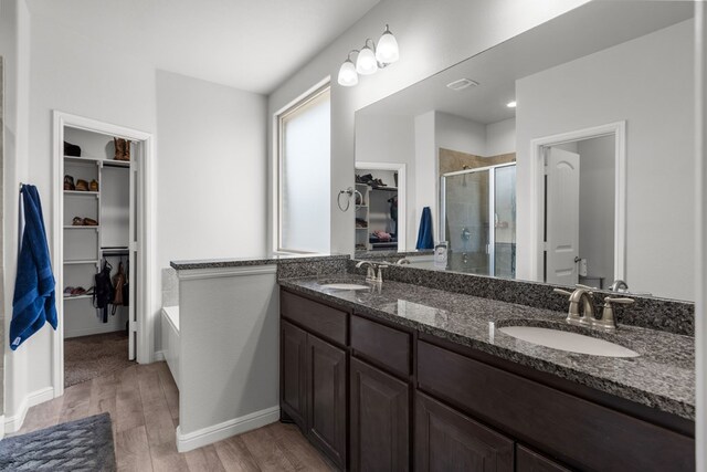 full bathroom with a stall shower, wood finished floors, a spacious closet, double vanity, and baseboards