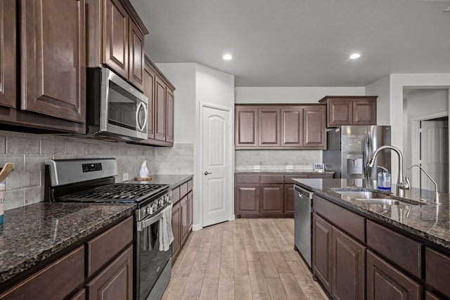 kitchen featuring appliances with stainless steel finishes, a sink, dark stone counters, light wood finished floors, and backsplash
