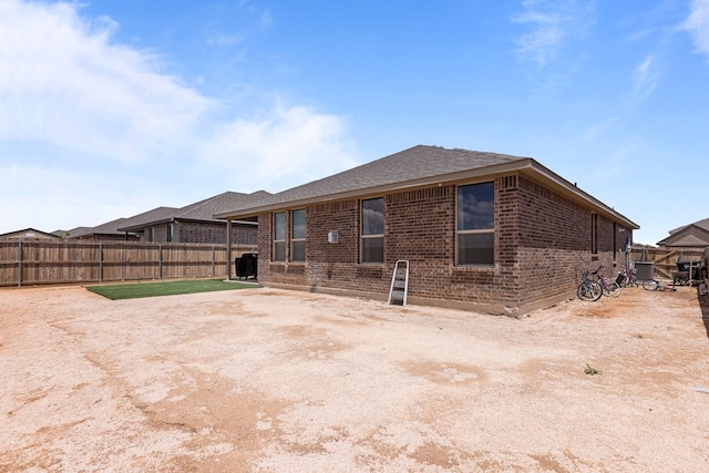 rear view of property featuring fence, brick siding, and roof with shingles