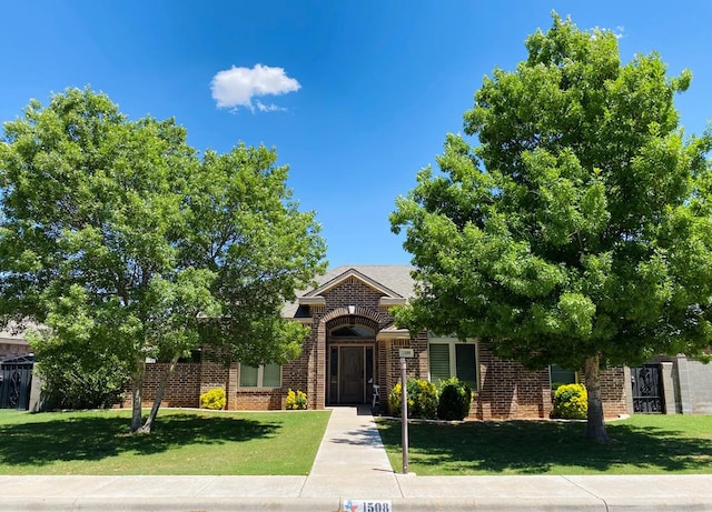 view of property hidden behind natural elements featuring brick siding and a front yard