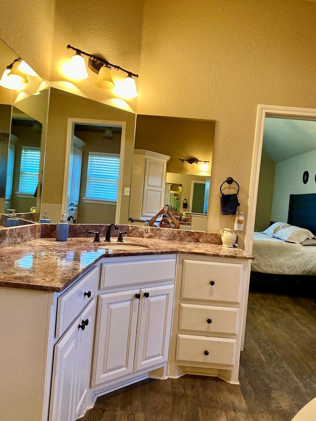 ensuite bathroom featuring a textured wall, ensuite bath, wood finished floors, and vanity