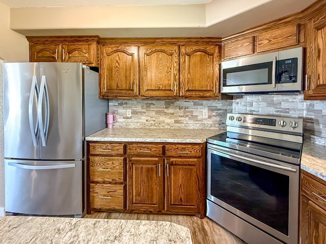 305 County Rd 306, Seminole, TX 79360 - kitchen featuring stainless steel appliances, brown cabinetry, light wood-style flooring, and tasteful backsplash