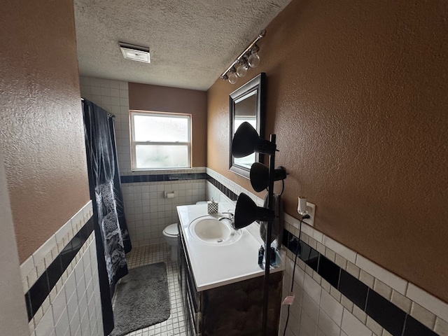 4417 Redbud Ave, Odessa, TX 79762 - full bathroom with tile walls, a textured wall, a textured ceiling, tile patterned flooring, and toilet