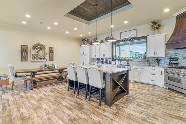 kitchen featuring high end range, white cabinets, a raised ceiling, light stone countertops, and a kitchen island