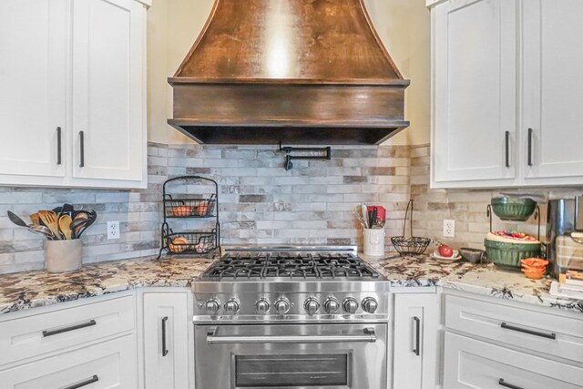 kitchen featuring stainless steel range, premium range hood, white cabinetry, and tasteful backsplash