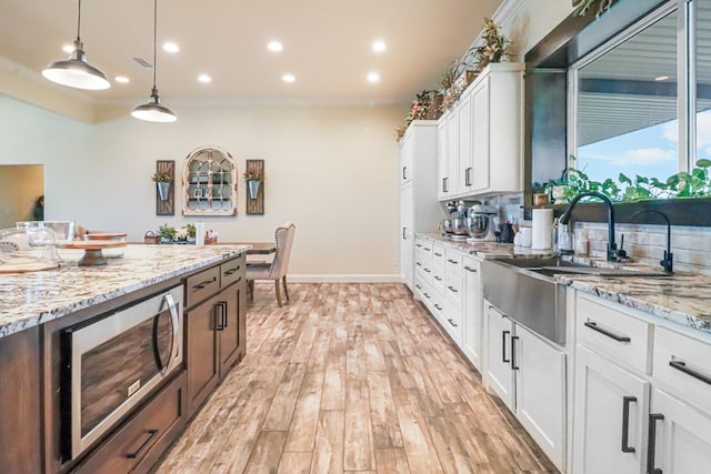 kitchen with light stone countertops, white cabinetry, stainless steel microwave, and ornamental molding