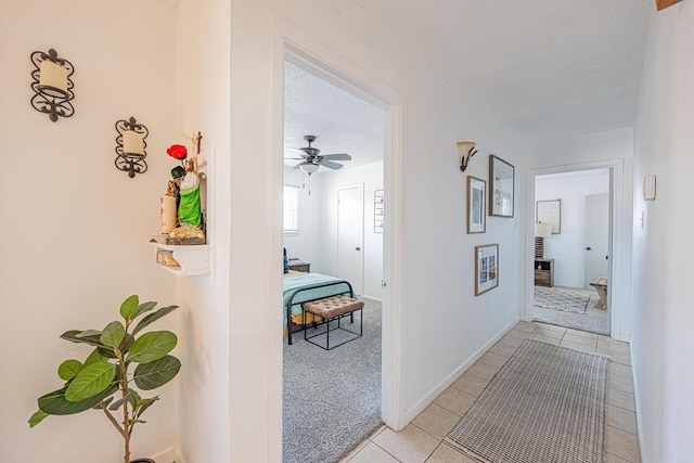 hall with a textured ceiling, light tile patterned floors, and baseboards