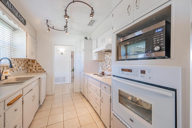 kitchen with white appliances, a sink, tasteful backsplash, under cabinet range hood, and a textured ceiling