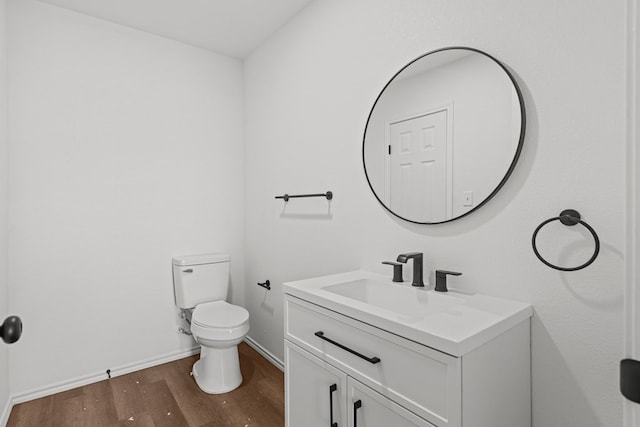 half bath with vanity, baseboards, wood finished floors, and toilet