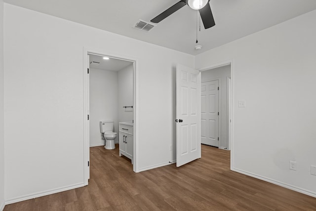 unfurnished bedroom featuring baseboards, connected bathroom, wood finished floors, and visible vents