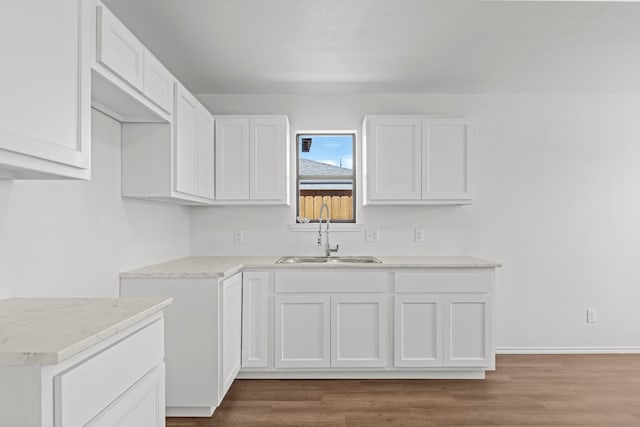 kitchen with baseboards, a sink, wood finished floors, and white cabinets