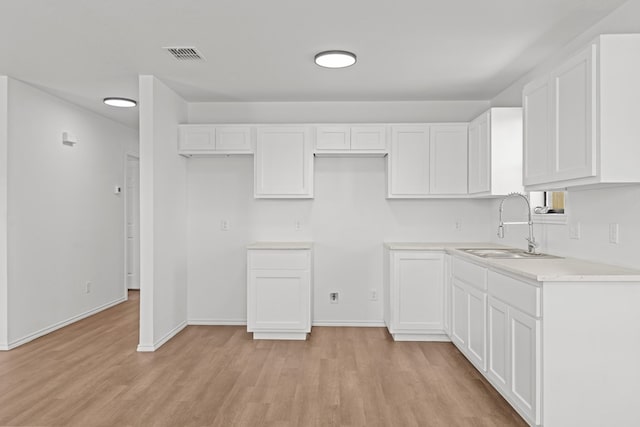 kitchen with visible vents, light countertops, white cabinets, a sink, and light wood finished floors