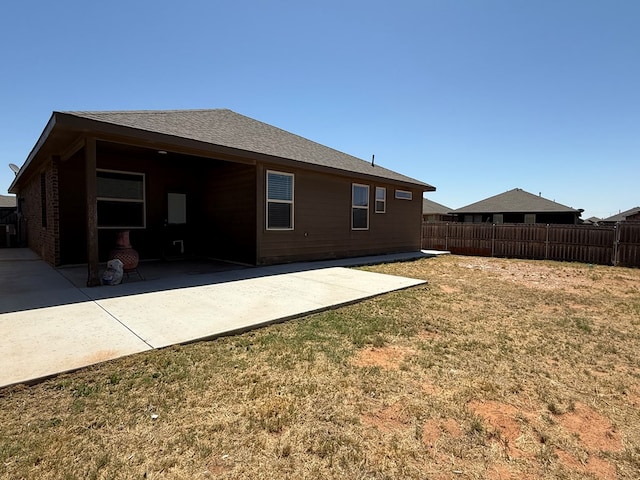 back of property featuring a lawn, a patio area, fence, and roof with shingles