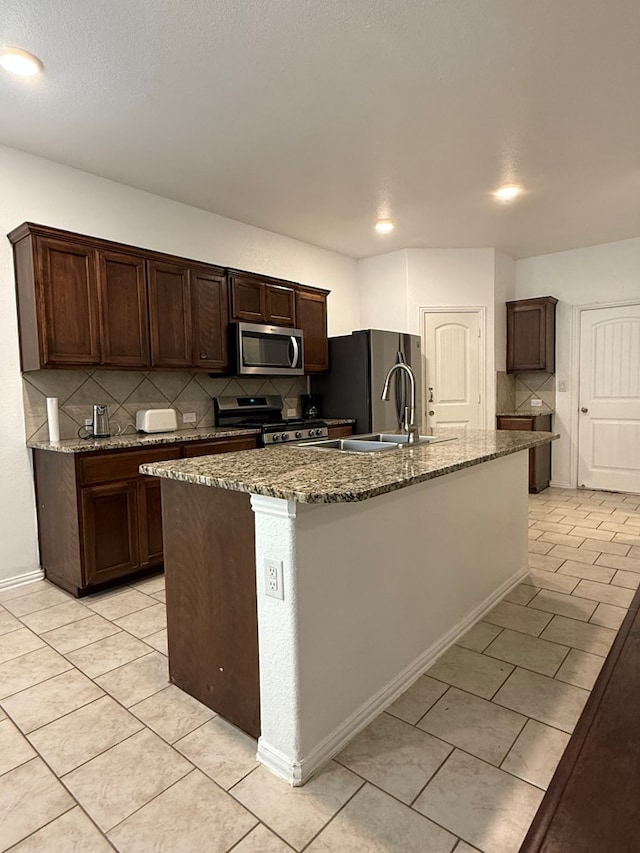 kitchen with tasteful backsplash, a center island with sink, light tile patterned floors, dark stone counters, and stainless steel appliances