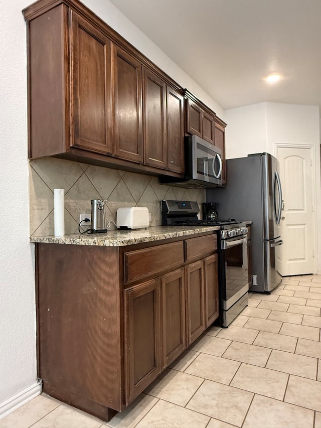 kitchen with dark brown cabinetry, backsplash, baseboards, stainless steel appliances, and light tile patterned flooring