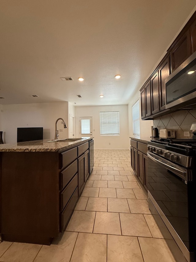 kitchen featuring dark brown cabinetry, stone countertops, tasteful backsplash, a sink, and stainless steel appliances