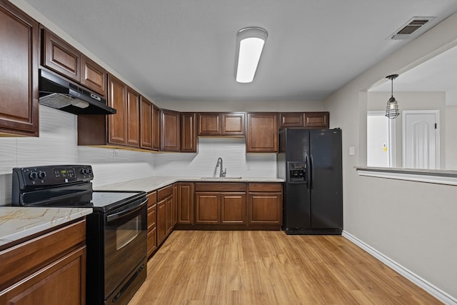 kitchen featuring light stone countertops, sink, hanging light fixtures, black appliances, and light wood-type flooring