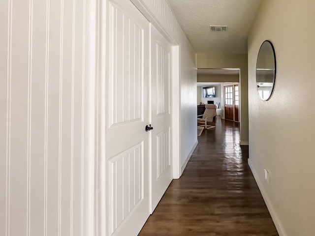 hall featuring a textured ceiling, dark wood-type flooring, visible vents, and baseboards