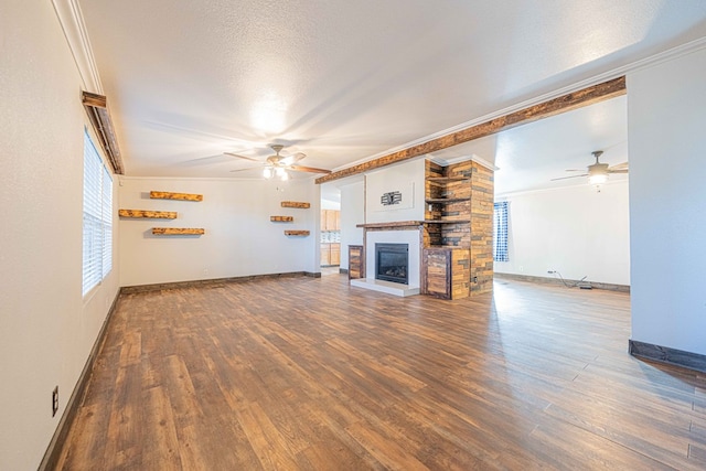 unfurnished living room with ceiling fan, a large fireplace, dark hardwood / wood-style flooring, a textured ceiling, and crown molding