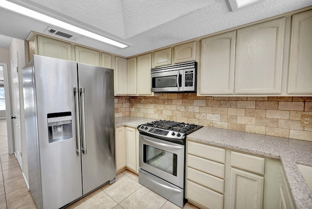 kitchen featuring appliances with stainless steel finishes, backsplash, cream cabinets, a textured ceiling, and light tile patterned flooring