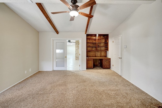 interior space with built in desk, lofted ceiling with beams, light carpet, a textured ceiling, and ceiling fan