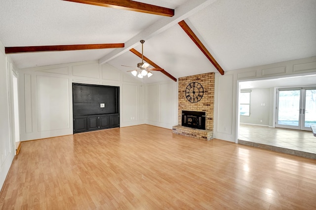 unfurnished living room featuring a brick fireplace, vaulted ceiling with beams, a textured ceiling, and light wood-type flooring