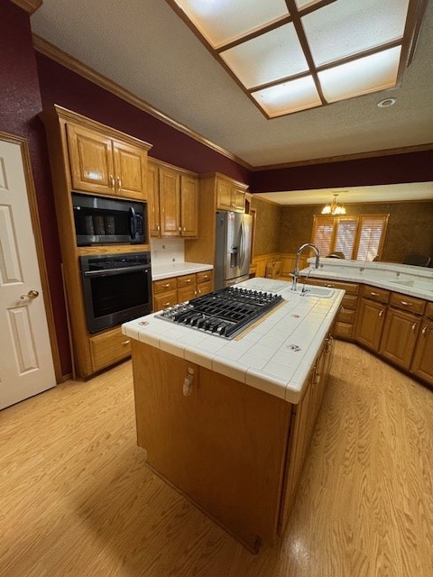 kitchen with sink, black appliances, a chandelier, tile counters, and an island with sink