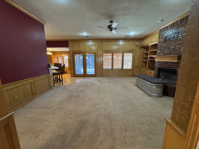 unfurnished living room featuring light carpet, built in shelves, a textured ceiling, and a brick fireplace