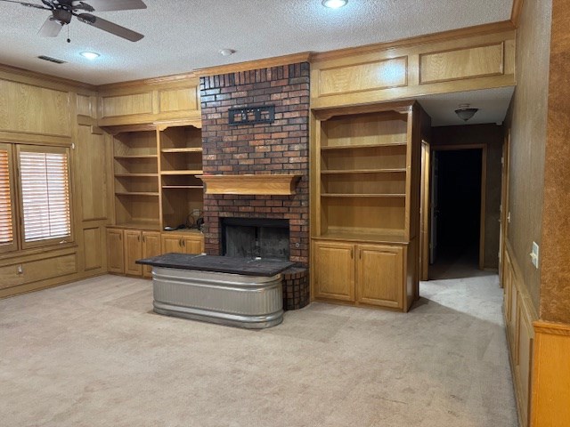 carpeted living room with wooden walls, a fireplace, ceiling fan, and a textured ceiling