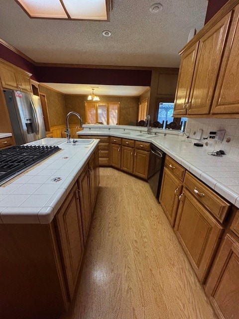 kitchen featuring a center island with sink, sink, light hardwood / wood-style flooring, tile counters, and stainless steel appliances