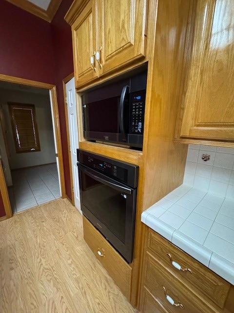 kitchen with decorative backsplash, tile counters, black appliances, and light hardwood / wood-style floors