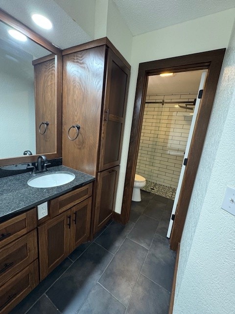 bathroom featuring a tile shower, vanity, a textured ceiling, and toilet