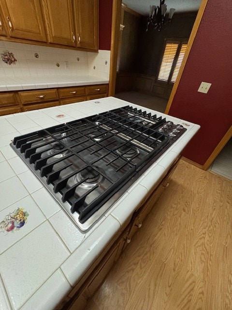 details with decorative backsplash, light wood-type flooring, tile counters, stainless steel gas cooktop, and a chandelier