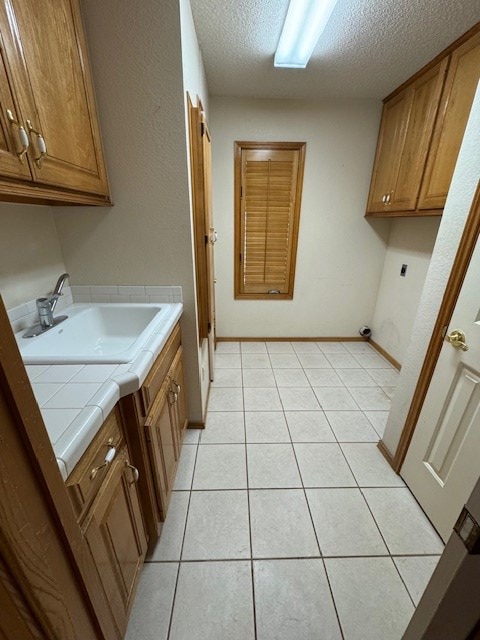 clothes washing area with sink, cabinets, electric dryer hookup, a textured ceiling, and light tile patterned flooring