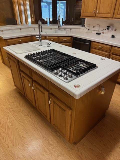 kitchen with stainless steel gas stovetop, a kitchen island with sink, light hardwood / wood-style floors, and black dishwasher