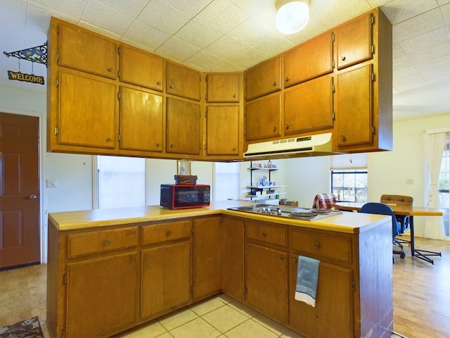 kitchen featuring kitchen peninsula, light tile patterned floors, and stainless steel cooktop