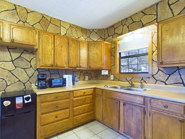 kitchen featuring light tile patterned flooring, black fridge, and sink