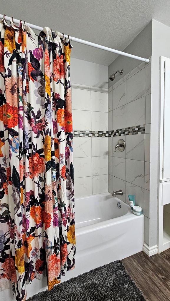 bathroom with hardwood / wood-style floors, a textured ceiling, and shower / tub combo