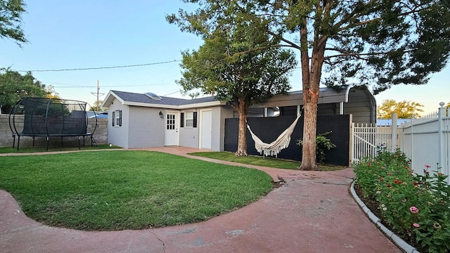 rear view of property featuring a trampoline and a lawn