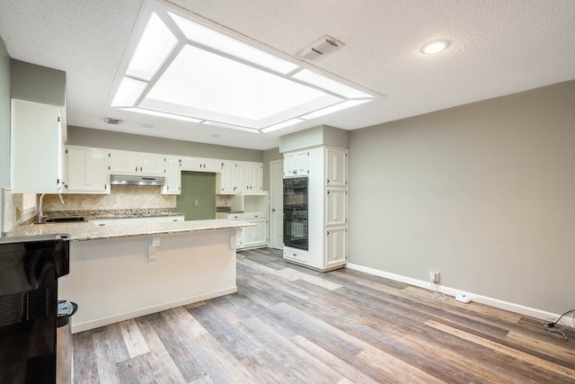 kitchen with kitchen peninsula, light hardwood / wood-style floors, white cabinetry, and light stone counters