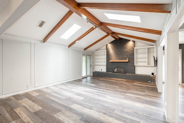 unfurnished living room featuring built in features, wood-type flooring, lofted ceiling with skylight, and a fireplace