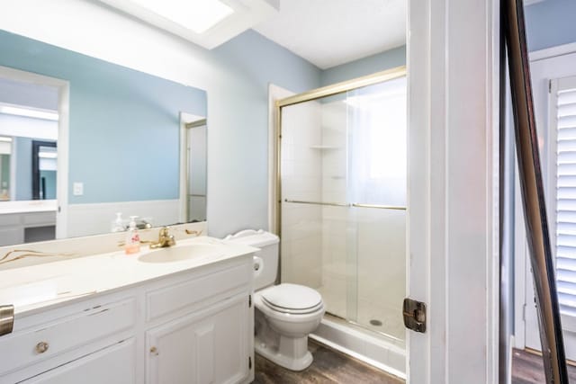 bathroom featuring wood-type flooring, vanity, toilet, and a shower with door