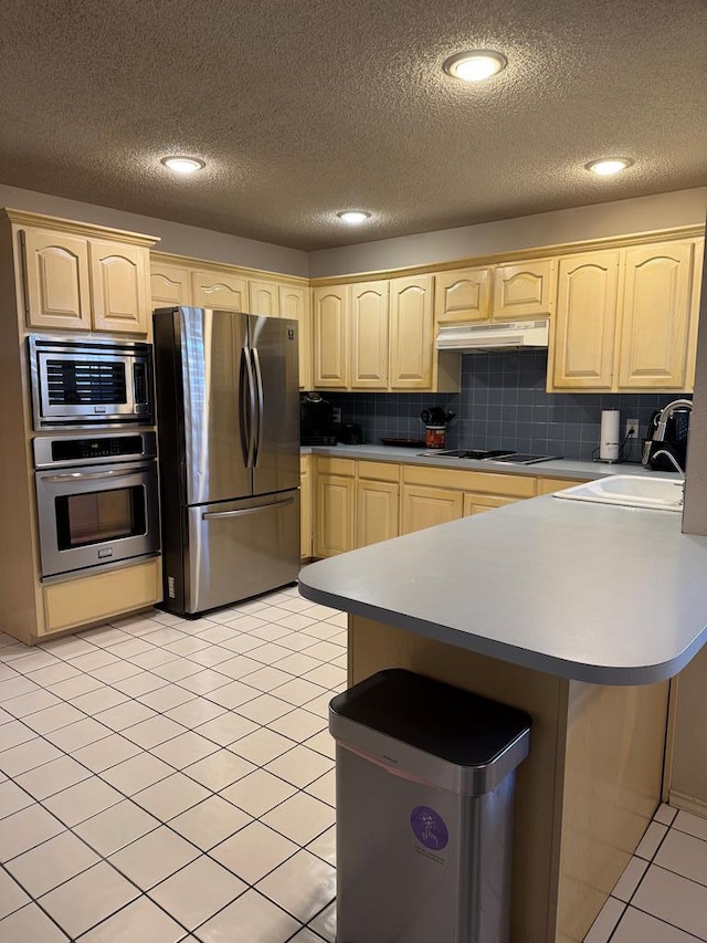 kitchen featuring sink, a textured ceiling, light tile patterned floors, decorative backsplash, and appliances with stainless steel finishes