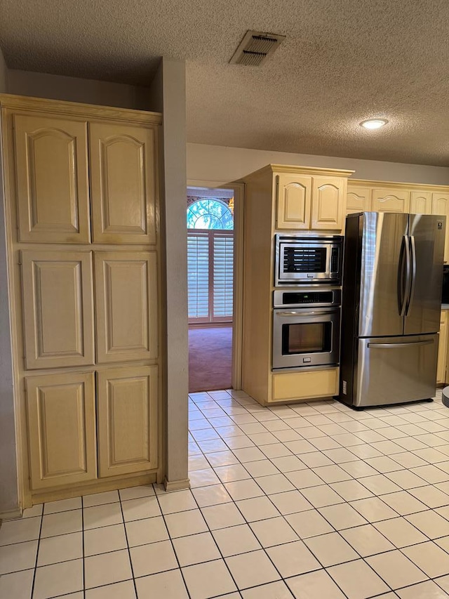 kitchen with light brown cabinets, stainless steel appliances, a textured ceiling, and light tile patterned flooring