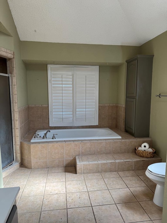 bathroom with tile patterned floors, toilet, a textured ceiling, vanity, and a relaxing tiled tub