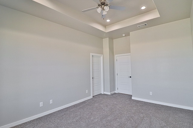 empty room featuring a tray ceiling, recessed lighting, visible vents, dark carpet, and baseboards