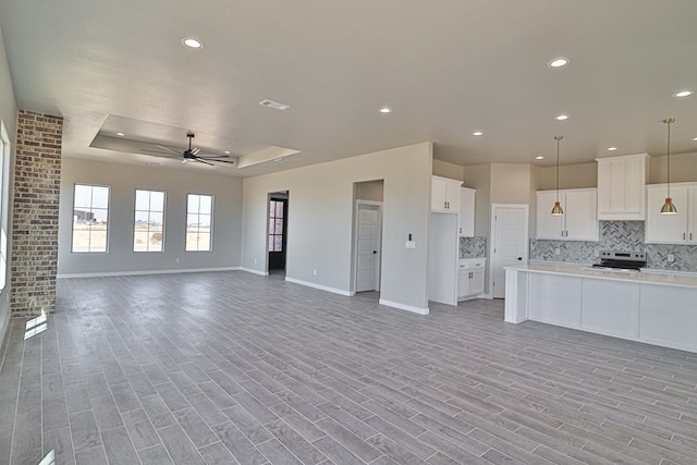 kitchen featuring a raised ceiling, backsplash, open floor plan, light wood-type flooring, and stainless steel electric range