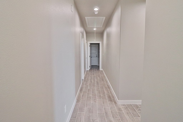 hall featuring attic access, wood tiled floor, and baseboards